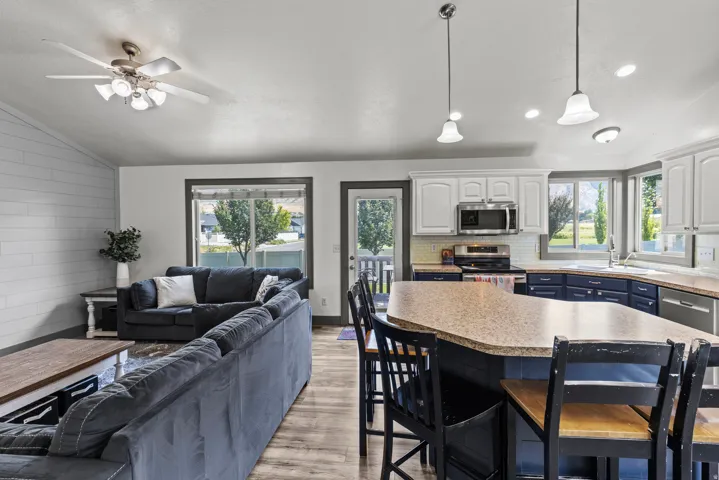 Open-concept living area featuring wood-finish flooring, a ceiling fan, and a kitchen with white upper and dark lower cabinetry