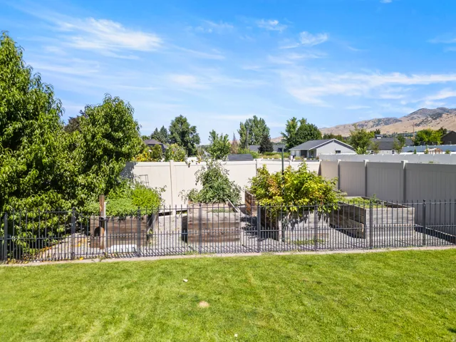 Expansive backyard featuring a manicured lawn, black metal fencing, raised garden beds, and mature trees