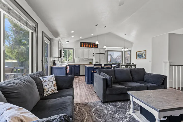 Open-concept living and kitchen area featuring vaulted ceilings with recessed lighting, navy cabinetry with stainless steel appliances, and expansive windows with natural light