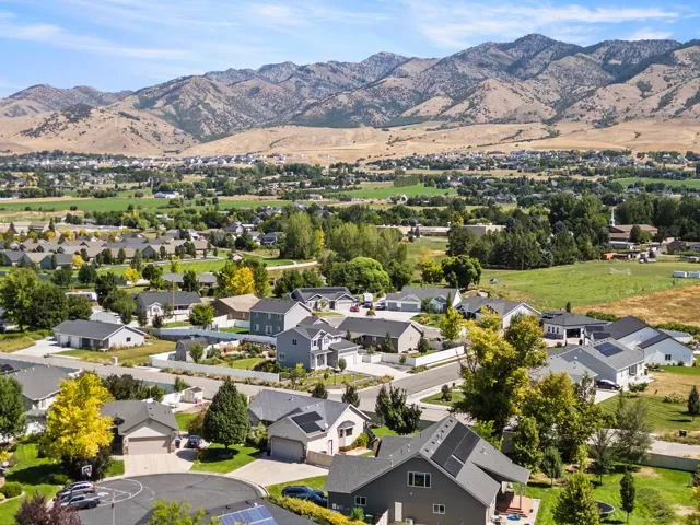 Aerial perspective showcasing a residential community nestled in a verdant valley, featuring mature landscaping, manicured lawns, and modern architectural homes with varied rooflines and neutral exterior finishes set against dramatic mountain backdrop