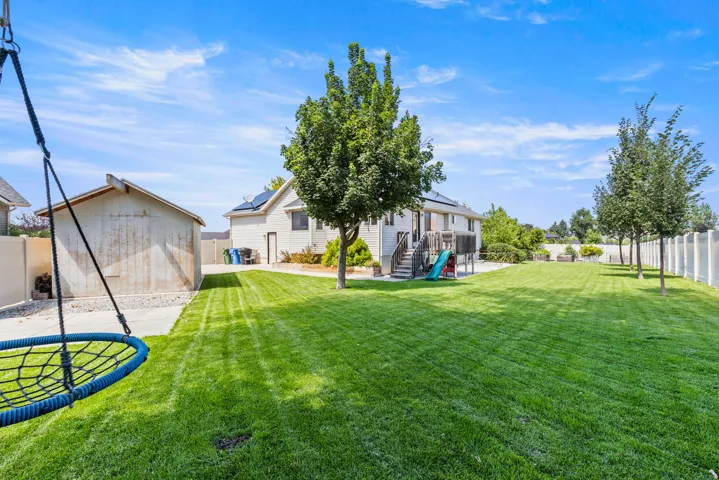Expansive manicured lawn with mature landscaping, detached garage, trampoline, and mature trees lining the property perimeter