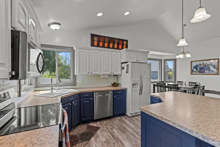 Chef's kitchen showcasing custom cabinetry in navy and white finishes, stainless steel appliances including a side-by-side refrigerator, and pendant lighting