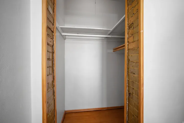 Hardwood flooring, exposed brick accents, white shelving, and a garment rod