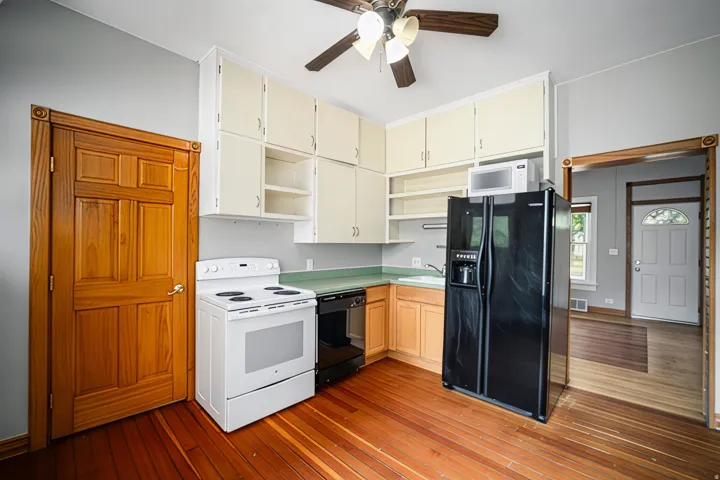 Kitchen featuring wood-finish flooring, white appliances, corner cabinetry, and a ceiling fan