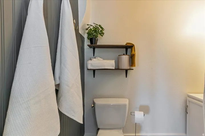 White toilet with a built-in toilet paper holder and two dark wood-finish floating shelves