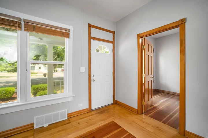 Hardwood flooring with contrasting wood inlay, white painted trim, natural wood door frames, and a white paneled front door with decorative glass
