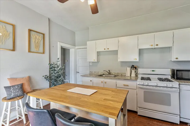 Wood-finish flooring, white cabinetry with gold-tone hardware, light-toned countertops, and a ceiling fan with integrated lighting