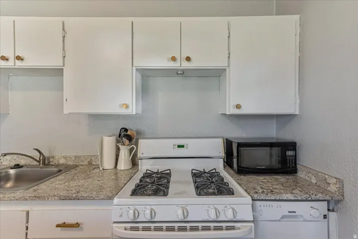 White upper and lower cabinetry, stainless steel sink, gooseneck faucet, white gas range, and light-toned countertop