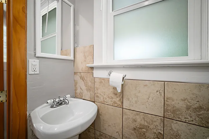 Pedestal sink with chrome faucet, light-toned wall tile, and a framed window