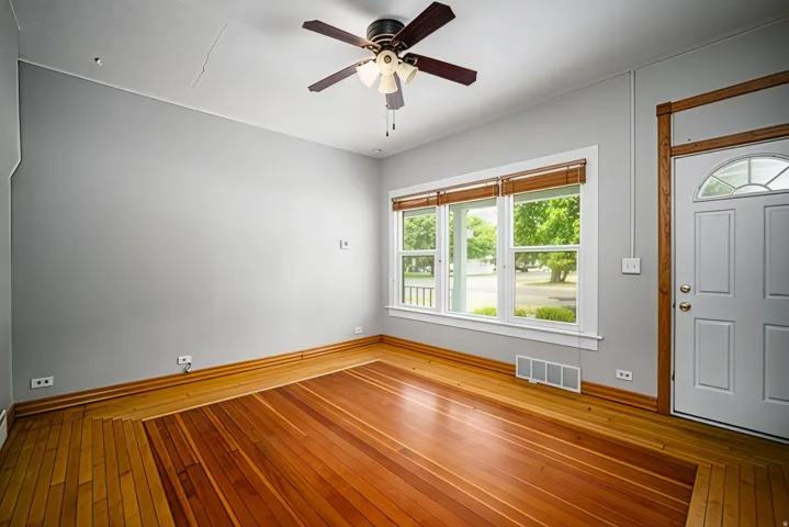 Wood-finish flooring, ceiling fan with light fixture, multiple windows with natural wood blinds, white paneled door with arched glass insert, and neutral wall tones