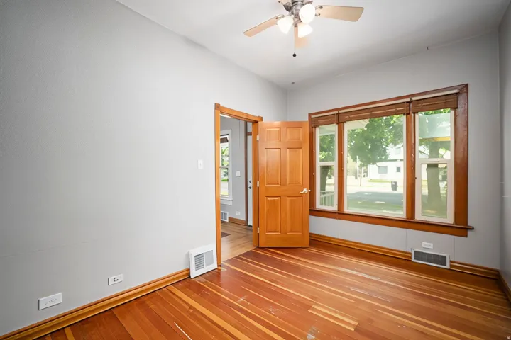 Hardwood flooring, natural wood trim, three-panel window, ceiling fan with integrated lighting, and a solid wood door