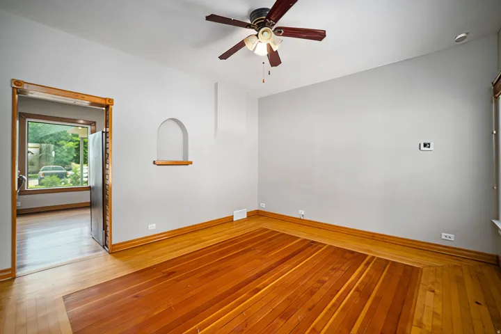 Hardwood flooring, arched wall niche, wood-trimmed doorway, ceiling fan, and window