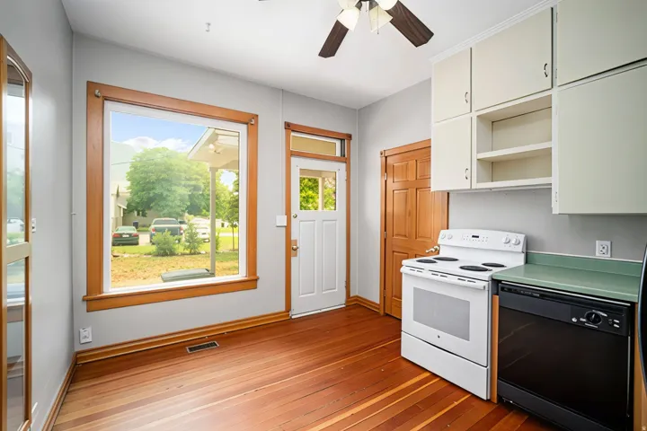 Wood-finish flooring throughout, bright window, white cabinetry, ceiling fan, and white freestanding range