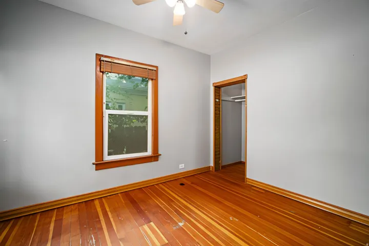 Wood-finish flooring, single window with wood trim, ceiling fan, and a built-in closet with shelving