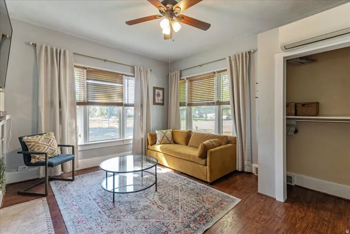 Wood-finish flooring, ceiling fan with integrated lighting, two windows with wood blinds, built-in open shelving, and a wall-mounted climate control unit