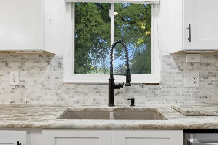 White shaker-style cabinetry, mosaic tile backsplash, black pull-down faucet, dual basin sink, and stone-finish countertops