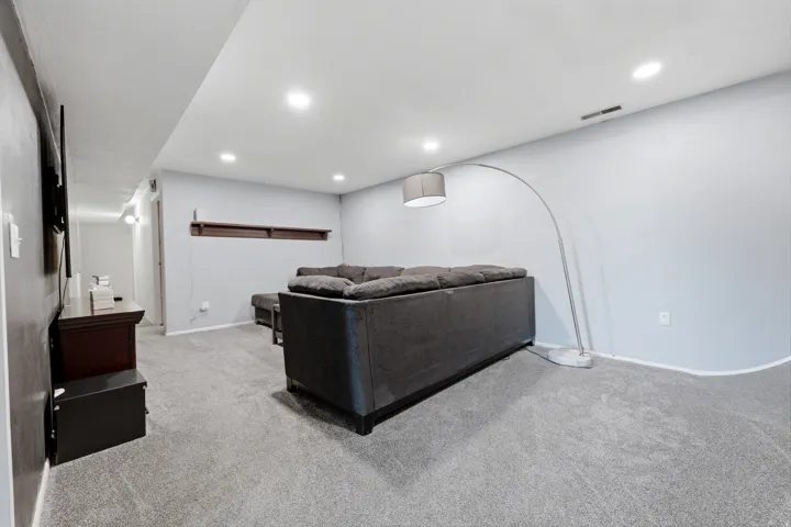 Recessed ceiling lighting, textured carpet flooring, light gray wall finish, and a built-in wall shelf