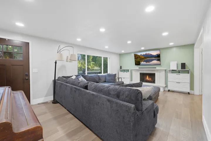 Recessed lighting illuminates this bright space featuring wood-finish flooring, a wood entry door with glass panels, and an integrated fireplace with a stone surround