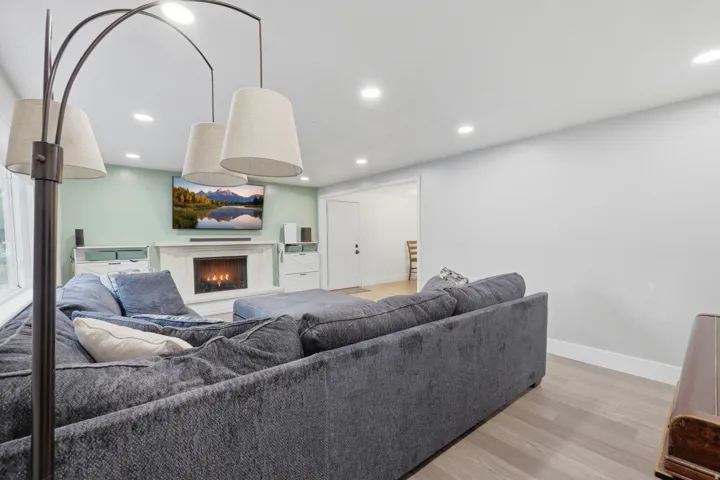 Recessed lighting, wood-finish flooring, and an electric fireplace with a white mantel and hearth
