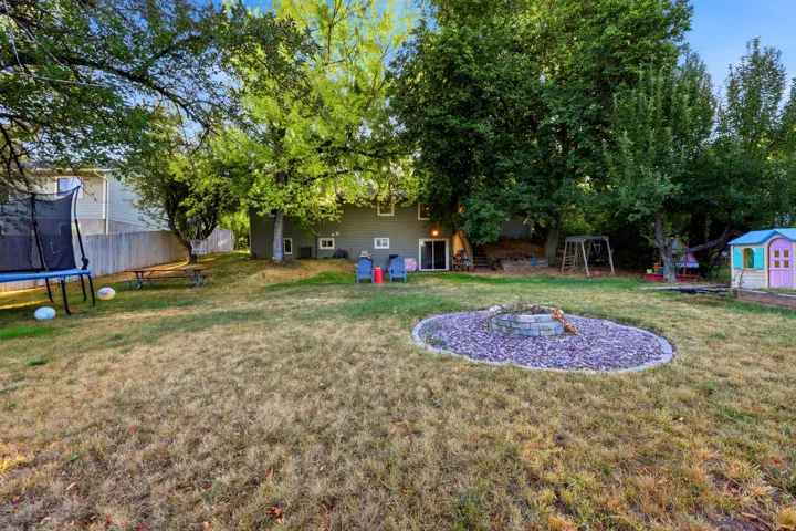 Expansive backyard featuring mature trees, a privacy fence, a ground-level patio, and a stone-edged fire pit area