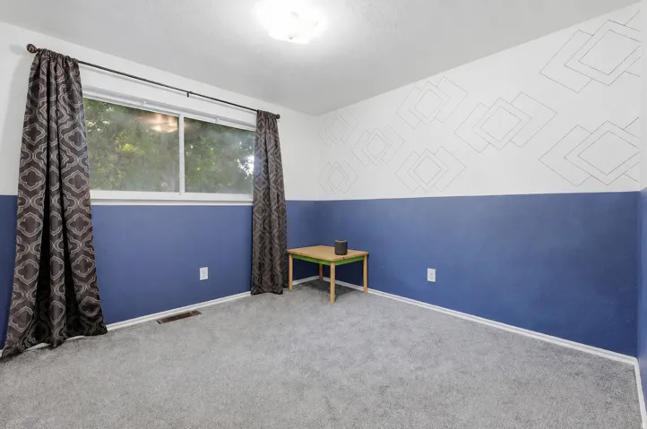Spacious bedroom featuring neutral carpet flooring, large picture window with natural light, and two-tone wall treatment with crisp white upper walls and rich blue lower walls