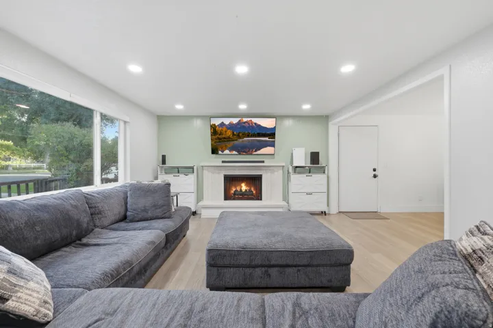 Recessed lighting, wood-finish flooring, large picture window, fireplace with white mantel, and open doorway