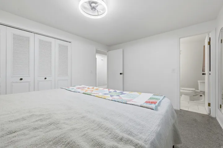 White walls, ceiling-mounted light fixture, louvered closet doors, carpeted flooring, and a white toilet