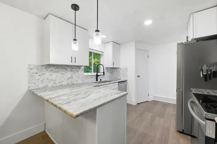 White cabinetry, stone-finish countertops, tile backsplash, wood-finish flooring, and pendant lighting