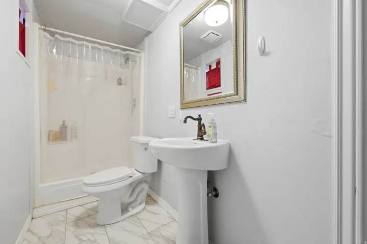 Pedestal sink with a bronze-finish faucet, framed mirror, and tiled flooring