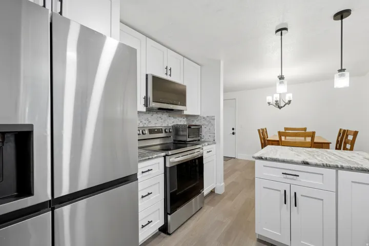 Contemporary kitchen featuring white cabinetry, stainless steel appliances, light-colored wood-finish flooring, and pendant lighting