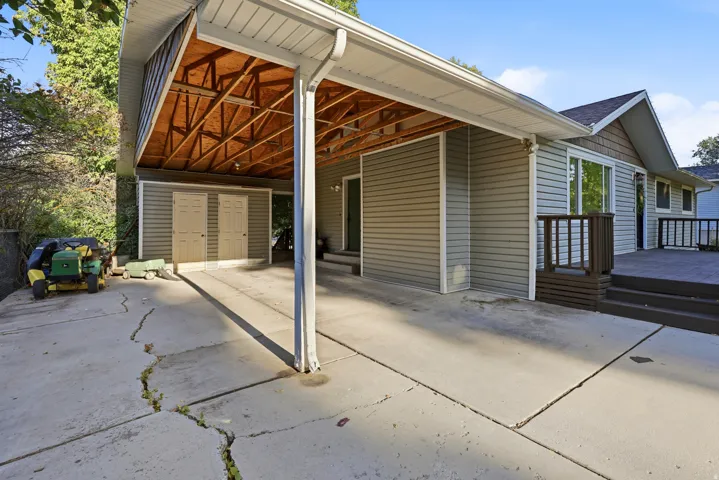 Covered carport with exposed wood ceiling beams, attached storage shed, and exterior siding