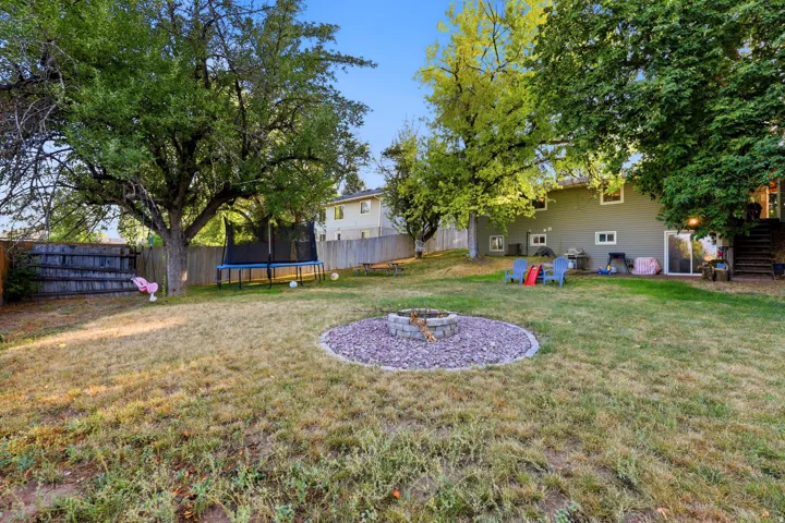 Expansive backyard featuring mature trees, a wood privacy fence, and a stone-rimmed fire pit area with gravel