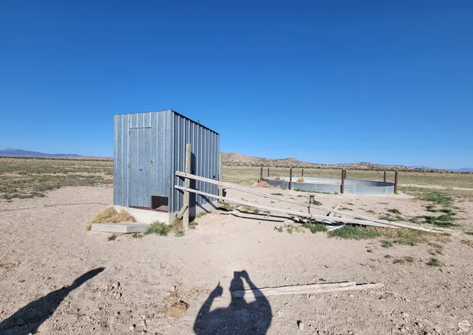 Corrugated metal structure on a concrete foundation, featuring an attached wooden fence