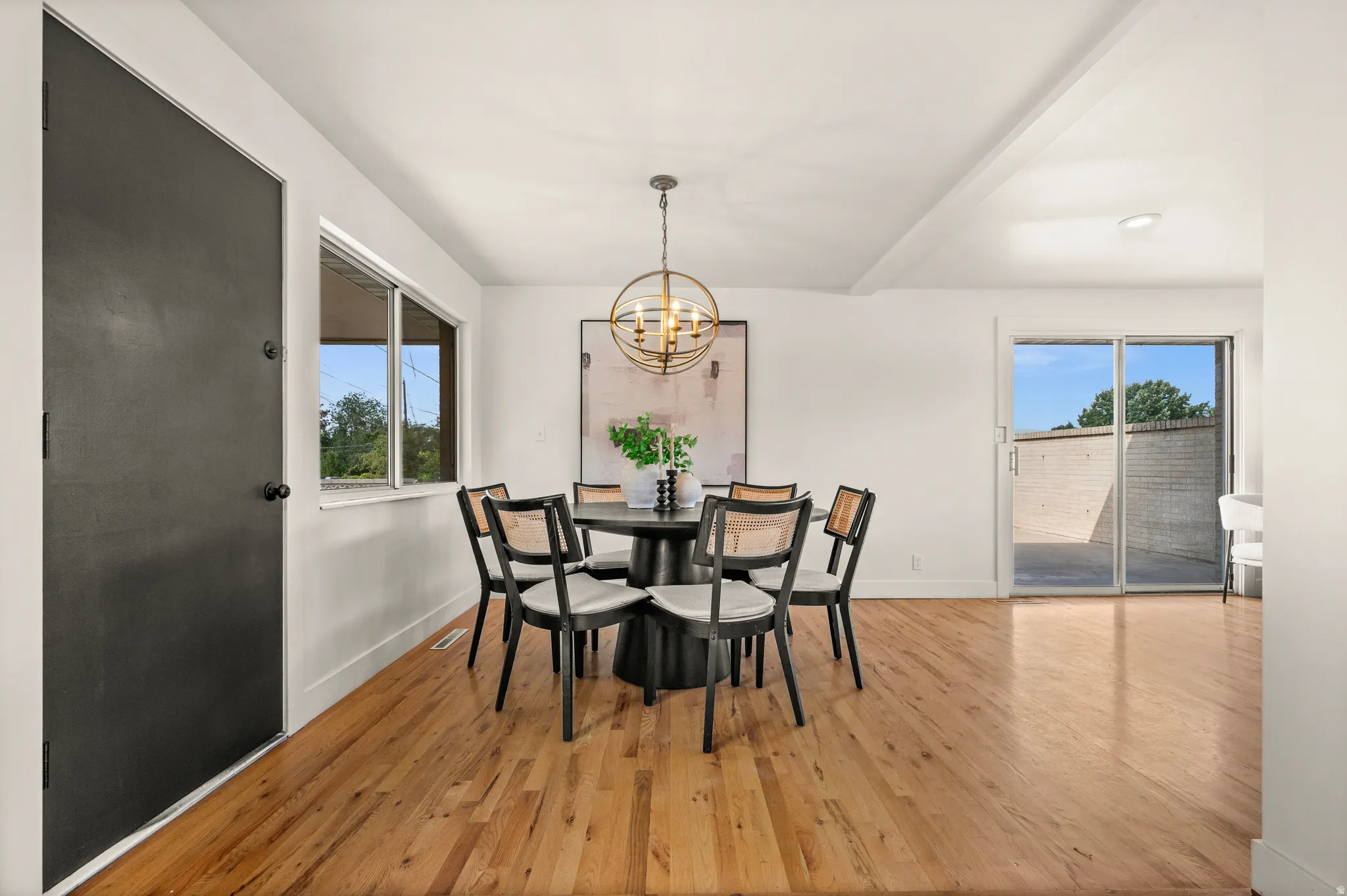 Bright dining area showcasing gleaming wood-finish flooring, abundant natural light from multiple windows, glass sliding doors opening to an outdoor patio, and a modern pendant fixture overhead