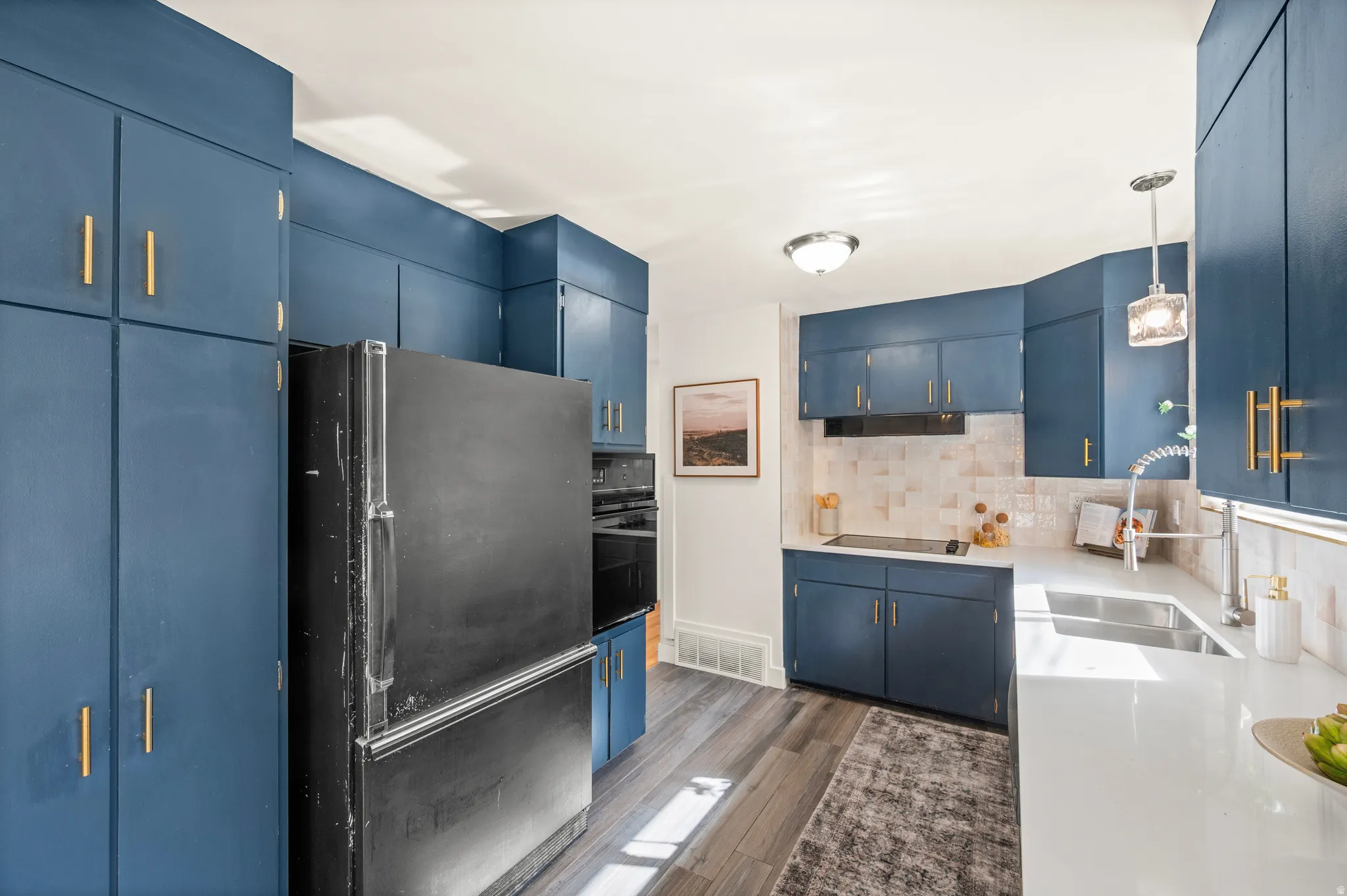 Modern kitchen featuring custom blue cabinetry with brass hardware, stainless steel French-door refrigerator, white subway tile backsplash, white quartz countertops, and a large center island with integrated sink and prep space