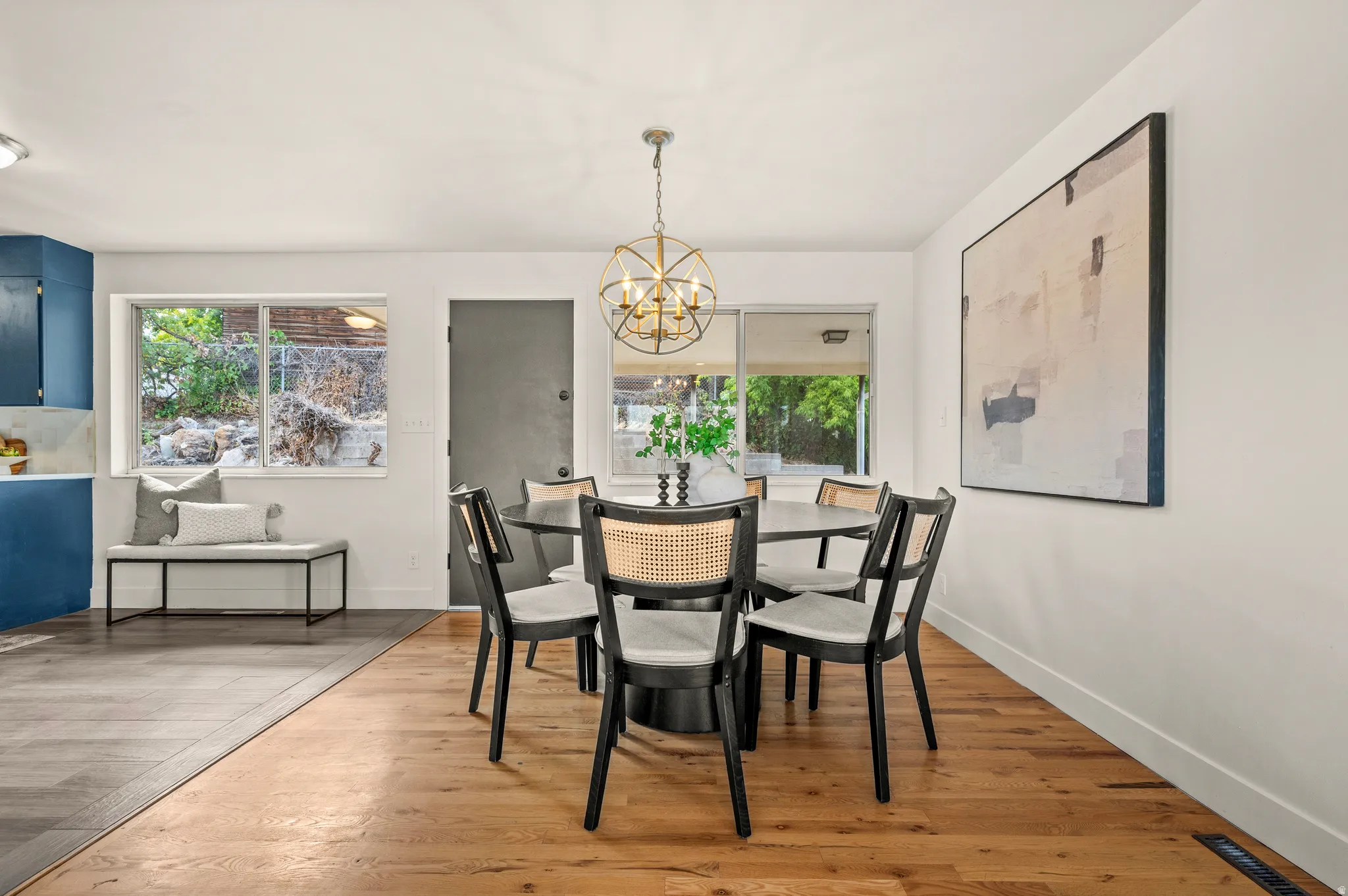 Bright dining area showcasing hardwood flooring, a round dining table with four black chairs, and geometric pendant lighting