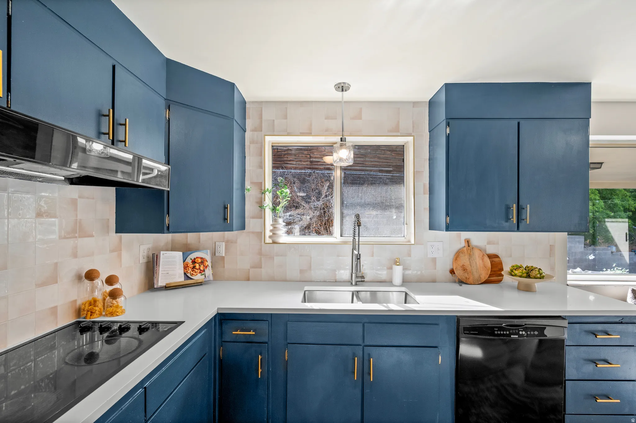 Modern kitchen featuring custom cabinetry in deep blue with brass hardware, stainless steel appliances including a black dishwasher, quartz countertops, a ceramic tile backsplash, and a stainless steel undermount sink with contemporary faucet