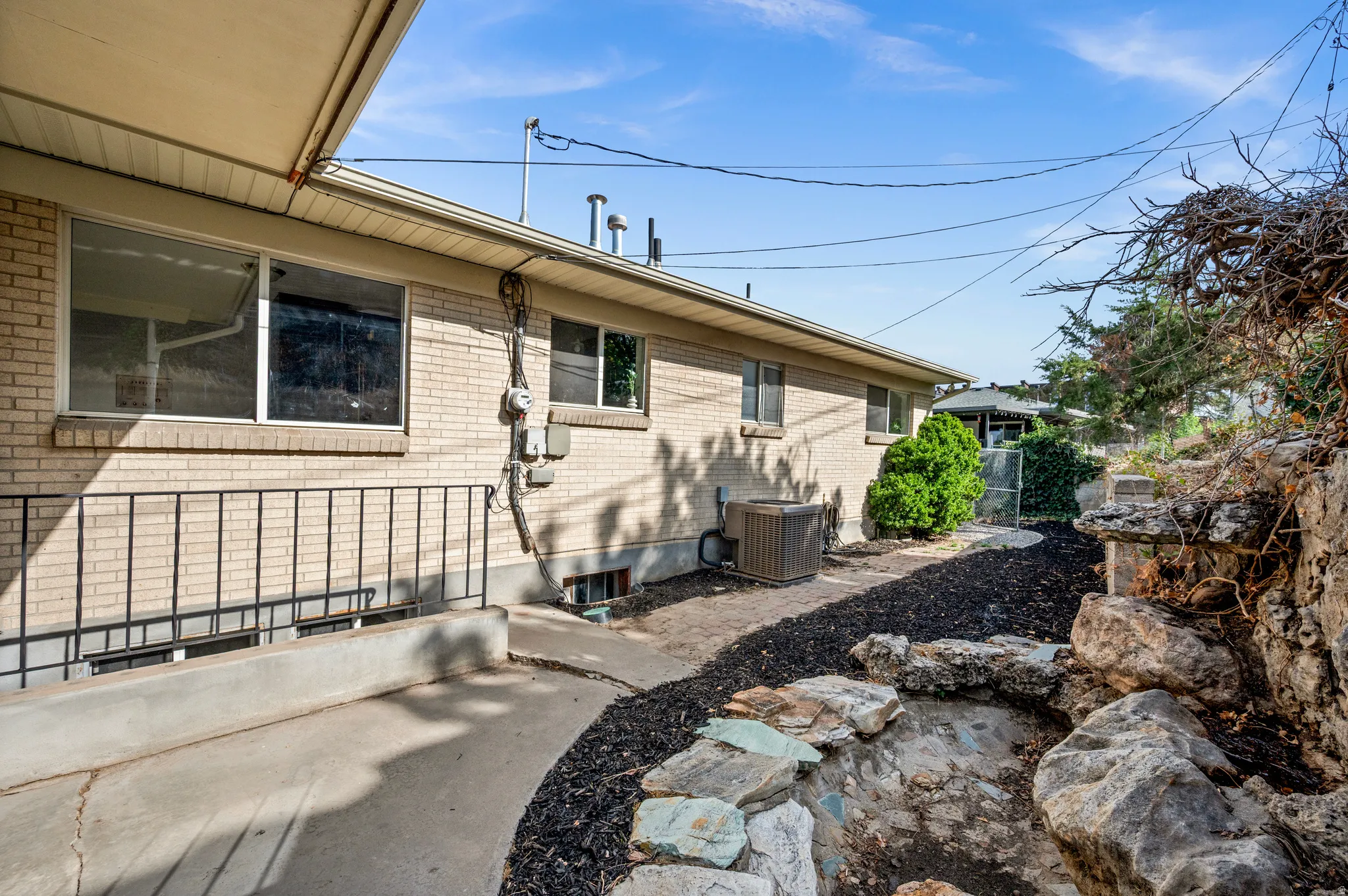 Brick residence with a contemporary landscaped front entrance featuring decorative black rock hardscaping, natural stone accents, and mature plantings