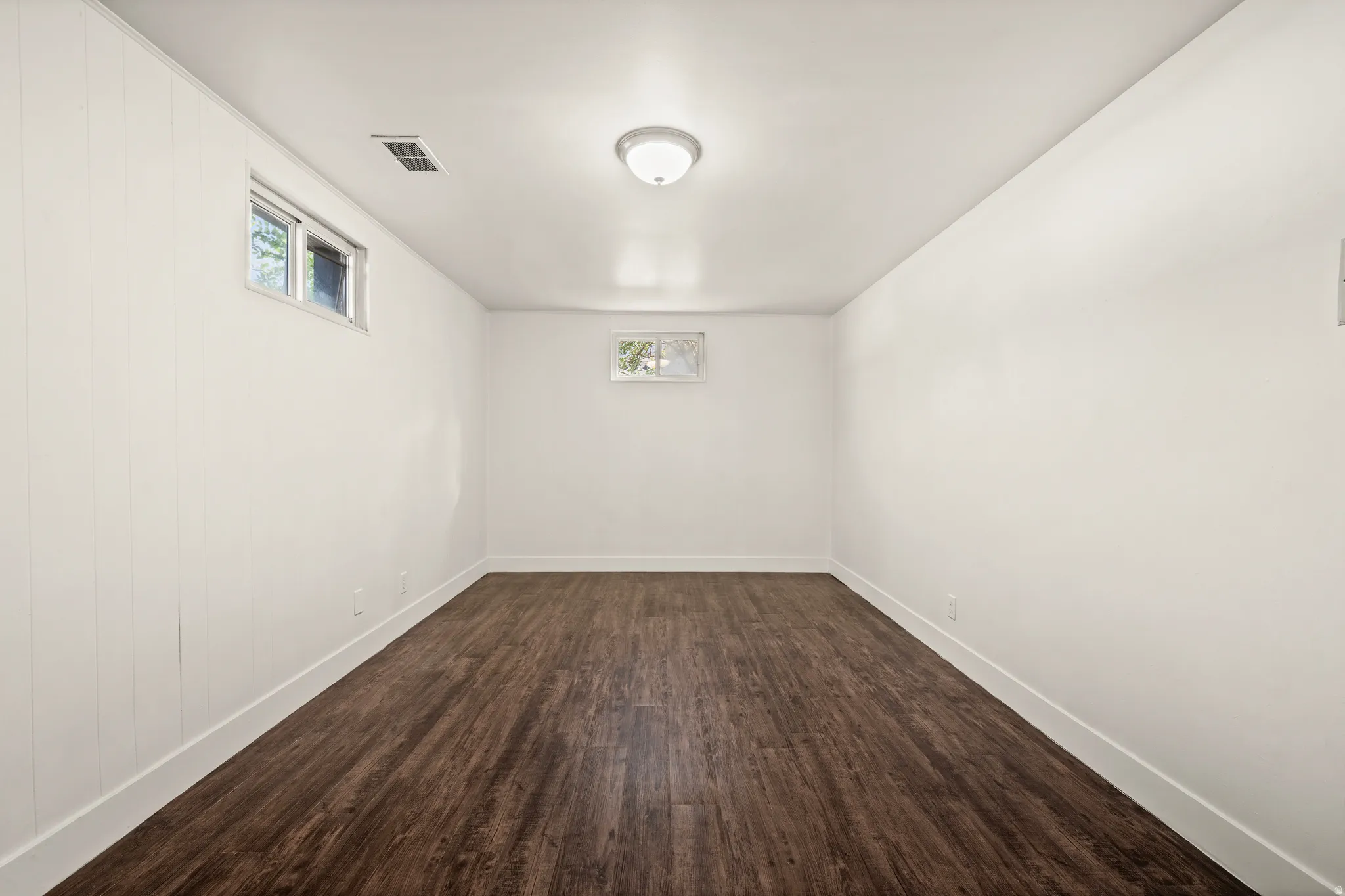 Spacious interior room featuring dark wood-finish flooring, white painted walls, and recessed ceiling lighting