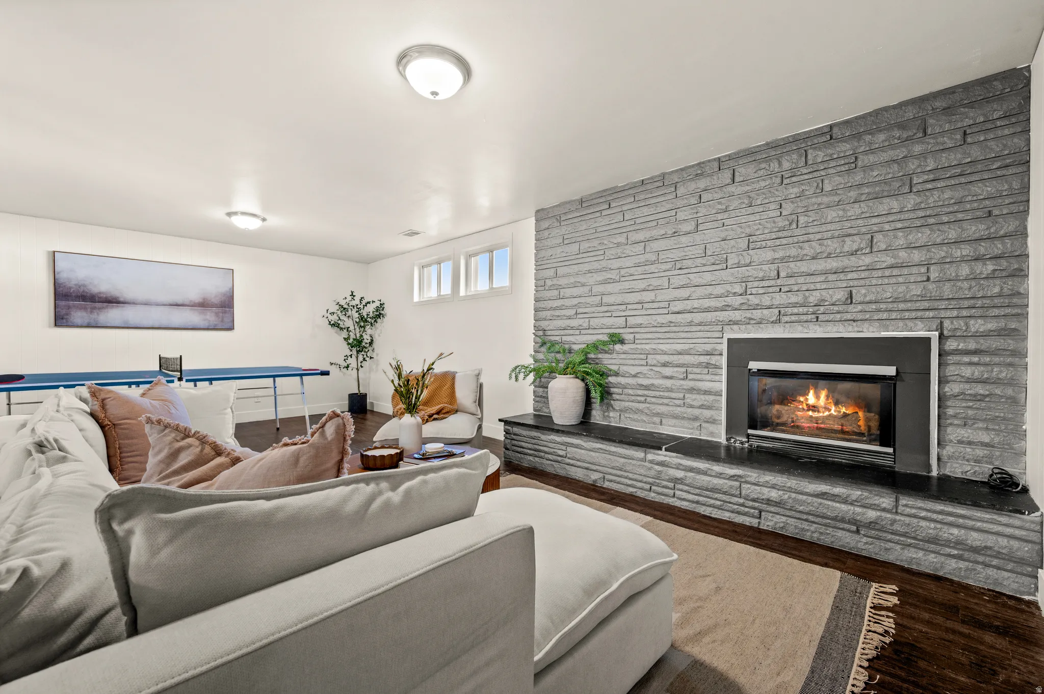 Stone accent wall with a built-in fireplace, dark wood-finish flooring, and multiple window openings