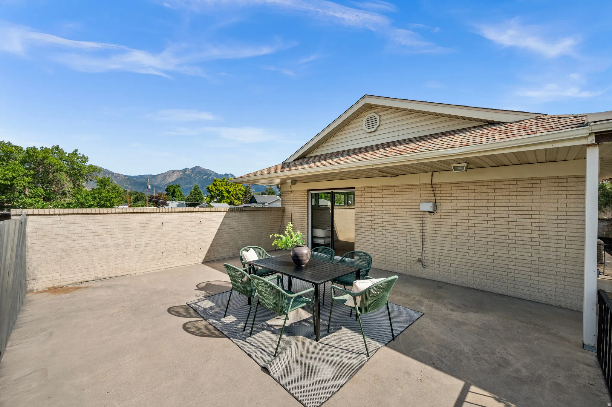 Expansive concrete patio with integrated dining area, framed by mature landscaping and mountain backdrop