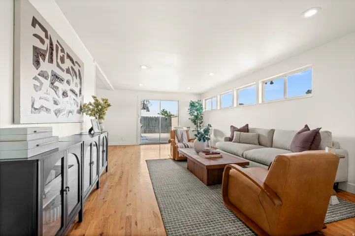 Bright, light-filled living area featuring expansive windows, warm wood-finish flooring, and custom cabinetry with black hardware