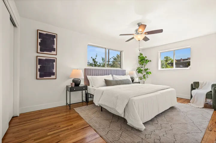 Bright primary bedroom showcasing hardwood flooring, ceiling fan with integrated lighting, and abundant natural light from multiple windows
