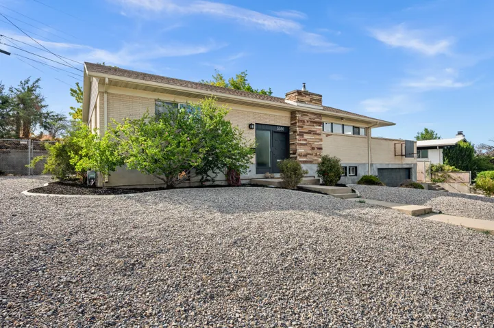 Modern mid-century residence featuring a clean-lined facade with brick and stucco exterior, expansive gravel forecourt with mature landscaping, and a geometric roofline with overhanging eaves