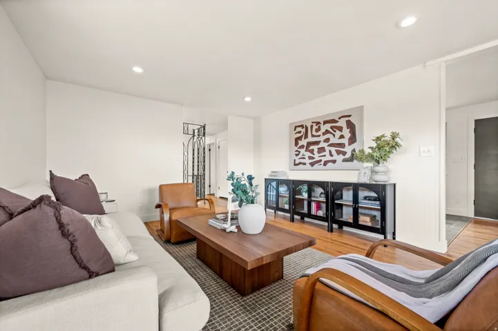 Bright, open living area featuring recessed ceiling lighting, white painted walls, and warm wood-finish flooring