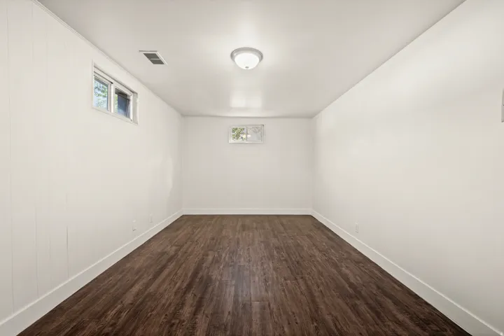 Spacious interior room featuring dark wood-finish flooring, white painted walls, and recessed ceiling lighting