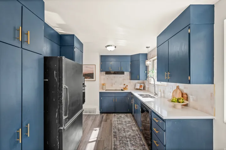Modern kitchen featuring custom blue cabinetry with brass hardware, white subway tile backsplash, and quartz countertops