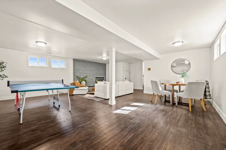 Expansive recreation room featuring dark wood-finish flooring, exposed support columns, and abundant natural light from multiple windows