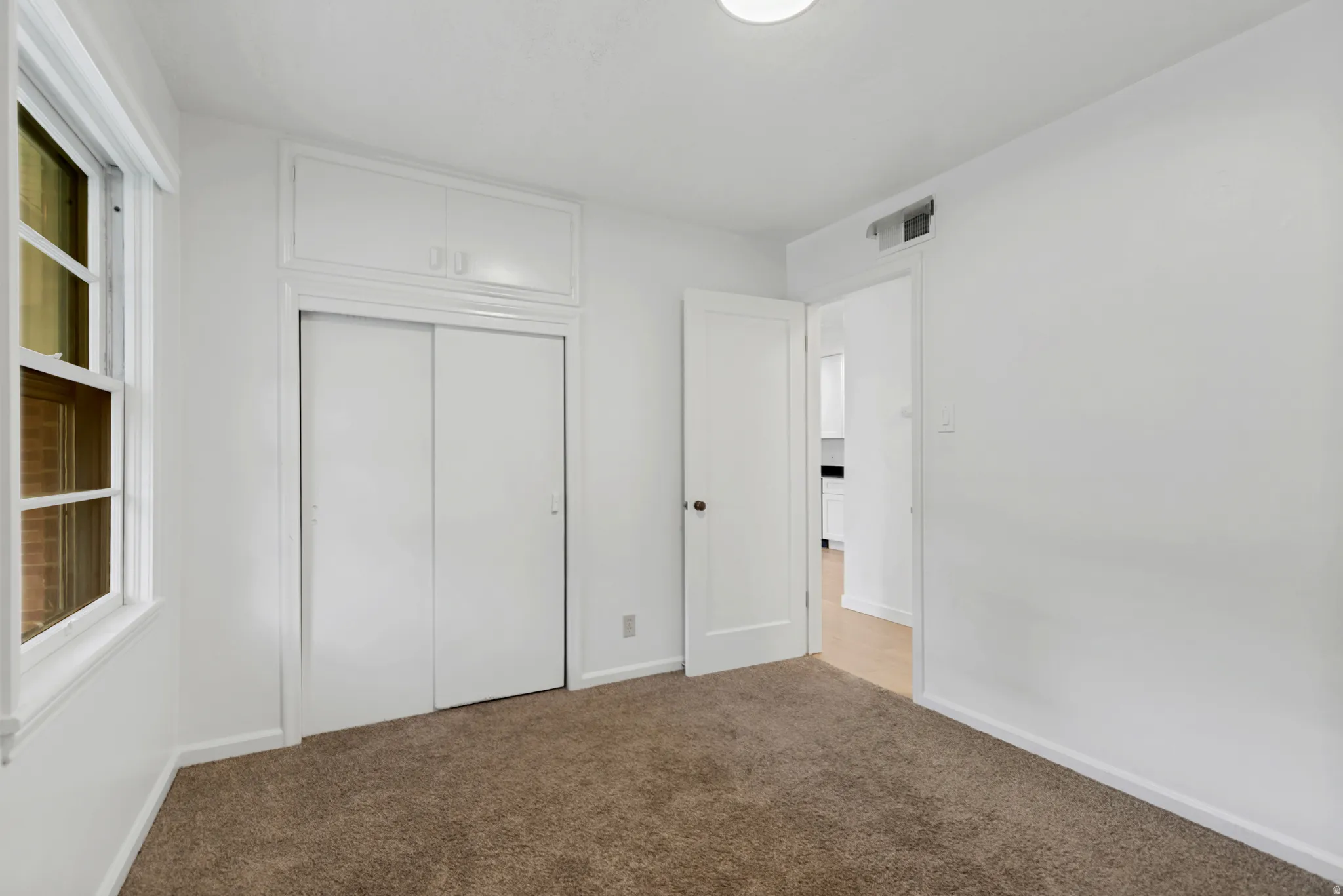White walls with a window, built-in cabinetry, and neutral carpeting