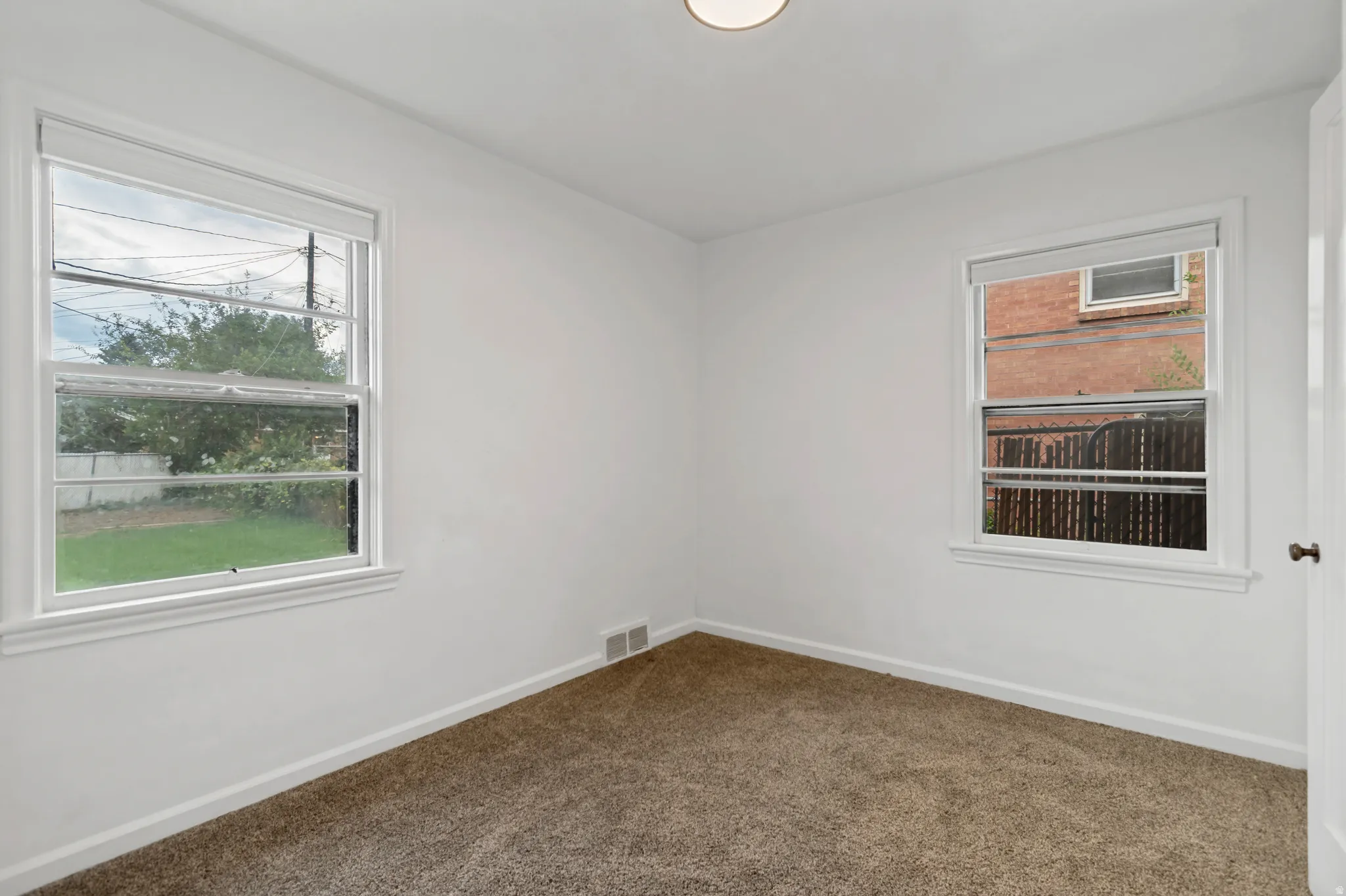 Bright secondary bedroom with carpet flooring, dual windows providing natural light, and clean white wall finishes